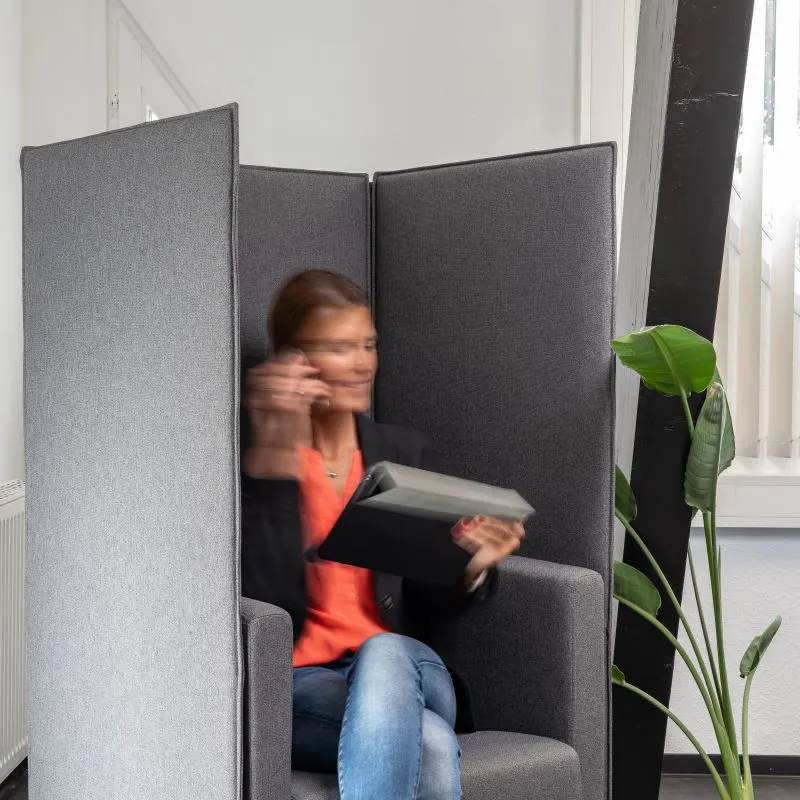 Ablenkungsfreier Fokusbereich im OG2 mit schallisolierenden Trennwänden, in dem eine Person konzentriert in einem komfortablen Sessel sitzt und telefoniert, umgeben von beruhigendem Grün einer Zimmerpflanze.